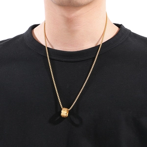 Close-up of men's gold cylinder pendant and box chain necklace worn over a black t-shirt