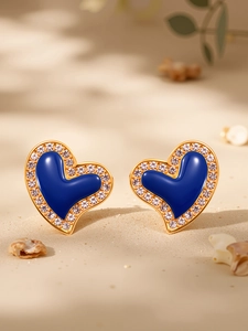 Macro detail of heart earrings with blue enamel, gold edges and white zircons on beach sand