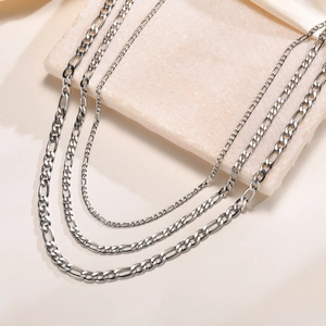 Detailed close-up of layered silver Figaro chain necklaces on a minimalist stone display