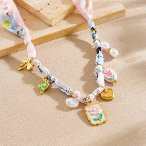 Close-up of floral silk ribbon necklace with gold heart, pearl, and flower charms