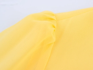 Close-up of yellow chiffon dress shoulder with pleated stitching and puff sleeve details