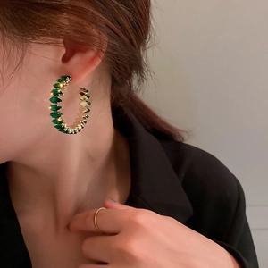 Close-up of a model wearing C-shaped gold earrings with rectangular green zircons