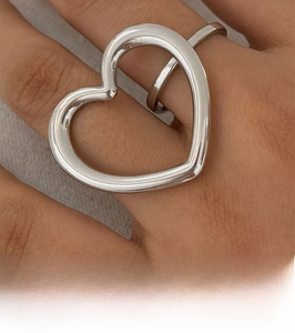 Detailed view of large hollow heart ring in silver finish worn on a finger