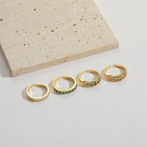 Close-up of gold open rings with green and clear gemstones on a stone surface