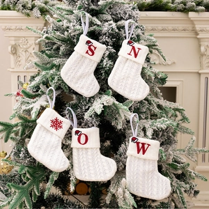 Close-up of white knitted Christmas stockings with red embroidered SNOW letters on tree