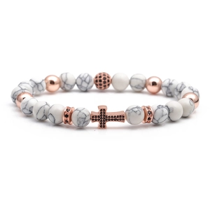 Macro shot of white turquoise beads and rose gold cross pendant with black zircon inlays
