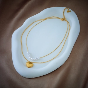 Double-layered necklace featuring a golden heart pendant and elegant white pearls on silk