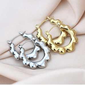 Detail of wavy gold and silver metal hoop earrings on soft pink fabric texture