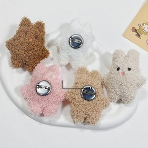 Plush star-shaped brooches in five colors with metal safety pins on a ceramic plate