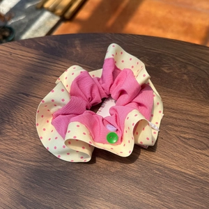 Detailed shot of pink and beige polka dot scrunchie with colorful buttons on wood