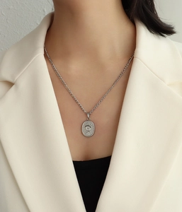 Gros plan d'un pendentif rose ovale en argent sur une chaîne Figaro et costume