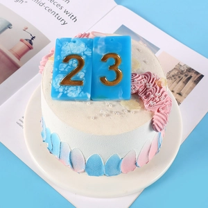 Close-up of blue and gold number 23 candle on a pink and blue frosted cake topper