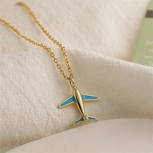 Macro shot of gold airplane pendant necklace with blue enamel details on soft fabric