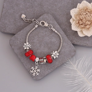 Detail of Christmas bracelet with red glass beads and snowflake charm on stone surface