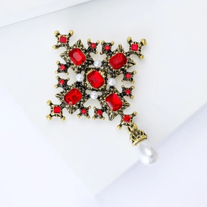 Macro detail of Baroque cross brooch with red crystal accents and pearl pendant drop