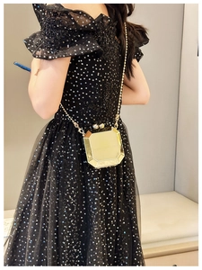 Close-up of elegant gold octagonal hard shell clutch bag paired with a black sequin dress
