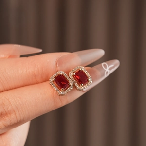 Detail of square halo earrings with red gemstone and rose gold finish on model