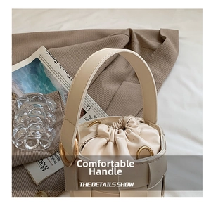 Close-up of beige woven bucket bag with wide leather straps and gold metal ring link