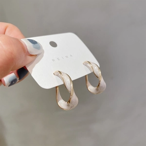 Gold-plated twisted hoop earrings with white enamel and pearls on a display card