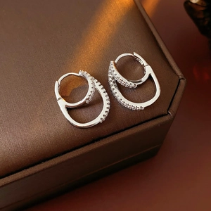 Close-up of elegant silver double hoop earrings with cubic zirconia on a textured surface
