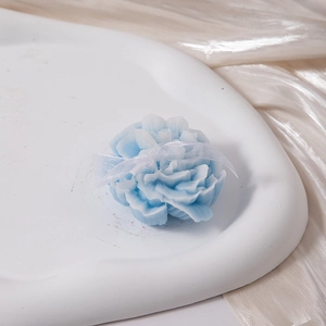 Detailed view of flower-shaped blue scented candle with white ribbon on a stone tray