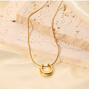 Close-up of golden U-shaped pendant on snake chain over beige stone and satin