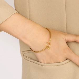 Close-up of minimalist gold cuff bracelet with round bead charm on a female wrist