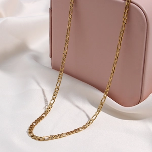 Dettaglio di una collana a catena Figaro dorata su seta bianca e scatola rosa