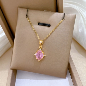 Close-up of golden necklace featuring a pink oval gemstone surrounded by white crystals