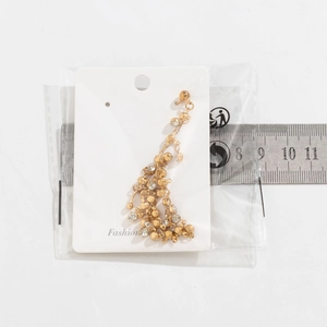 Detail view of gold tassel earrings with rhinestones next to a measuring scale