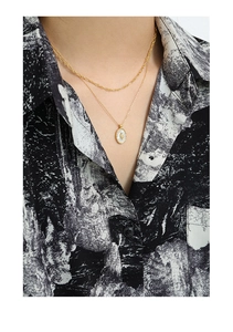 Detail view of double-layered gold necklace with oval tulip shell pendant on model