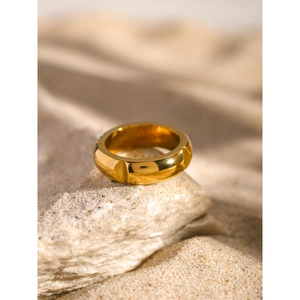 Close-up of minimalist 18k gold stainless steel ring on natural stone with sand background