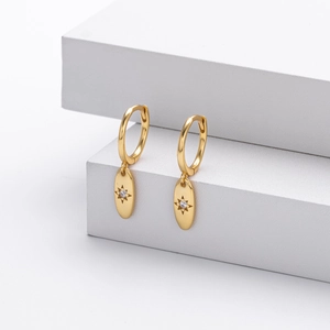 Detail of gold starburst engraved oval pendant earrings on white geometric stands