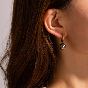 Minimalist gold hoop earrings with black sphere pendant worn on model's ear
