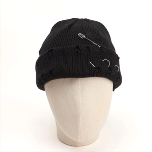 Detail of black knit beanie with distressed edges, safety pin and silver metal rings decoration