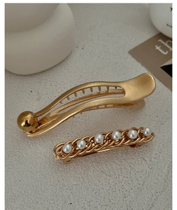 Close-up of golden hair clips with pearls and streamline design on beige texture