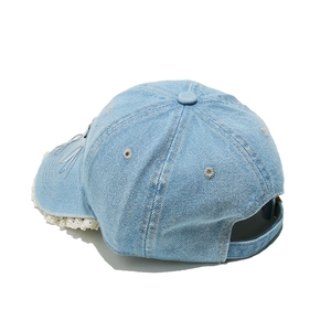 Détail de la casquette en jean bleu clair avec bordure en dentelle blanche et ruban argenté