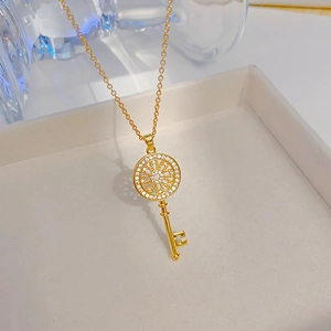 Elegant gold zircon key pendant necklace with floral design on a white jewelry box
