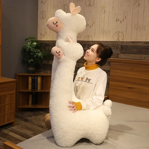 Giant white cartoon alpaca plush toy held by a model in a warm bedroom setting