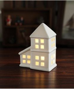 Close-up of white ceramic Christmas house ornament with warm LED light glowing inside
