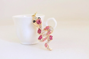 Detail of a golden snake keychain with pink and white rhinestones on a white surface