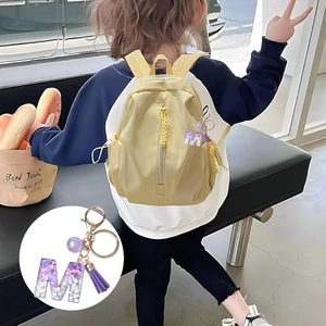 Sparkly purple glitter letter M keychain with tassel on a yellow backpack