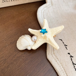 Close-up of starfish hair clip with white shell, pearl and blue crystal on fabric