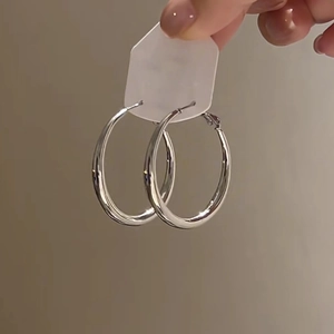 Close-up of polished silver hoop earrings held by hand against a clean solid background