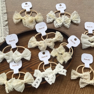 Nine pairs of lace bow hair scrunchies with pearls in creamy white on a wooden tray