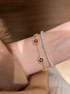 Close-up of gold flower bracelet with red zircons and dainty pearl chain stack