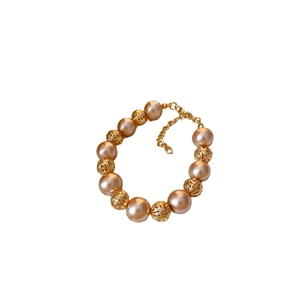 Bracelet en perles roses et billes d'or ajourées avec fermoir mousqueton sur fond blanc