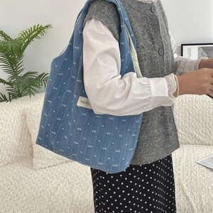 Sac fourre-tout en denim bleu avec motif nœud blanc porté à l'épaule dans un intérieur doux