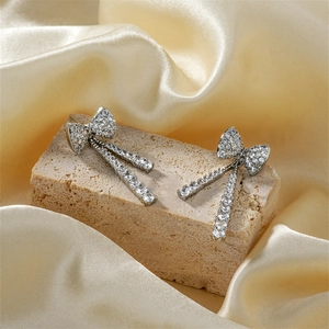 Exquisite silberne Schleifenohrringe mit langen Diamantquasten auf Seidenhintergrund
