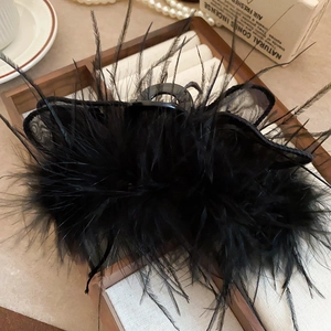 Close-up of black feather and mesh hair claw clip placed in a vintage wooden jewelry box